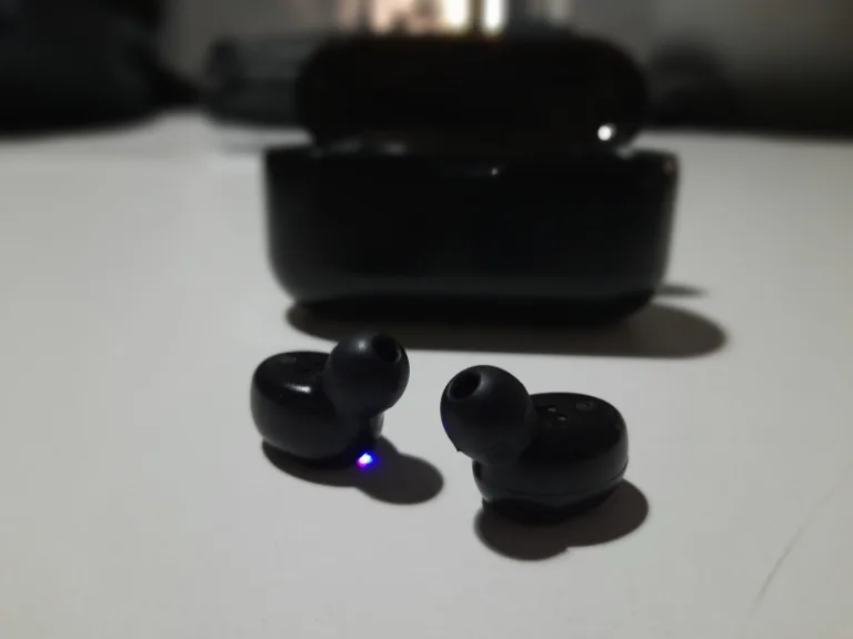 Small wireless earpieces beside their charging case on a table
