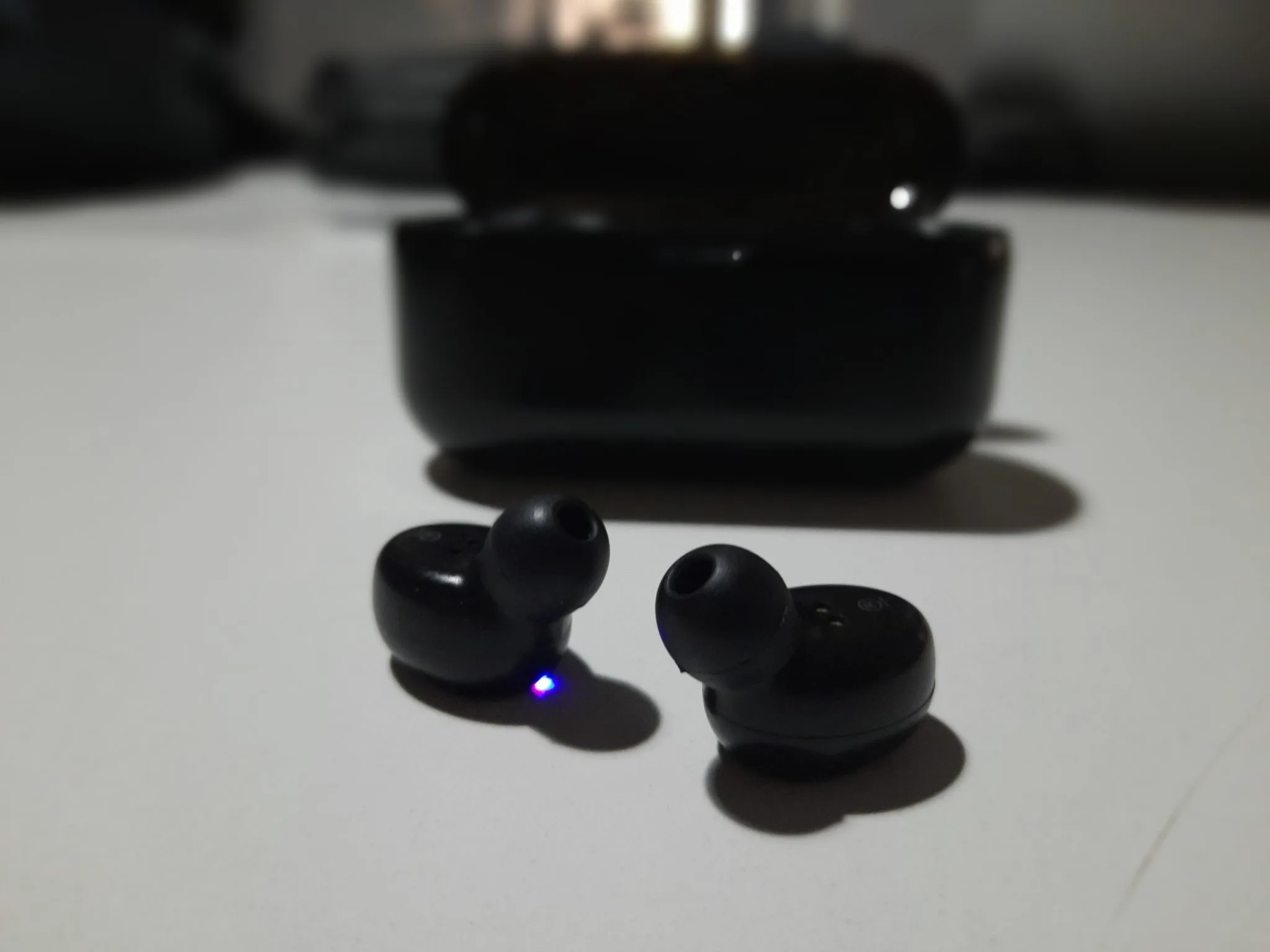 Small wireless earpieces beside their charging case on a table