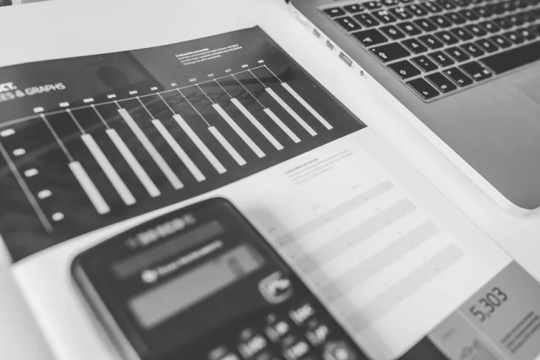 A calculator resting on financial papers beside a laptop