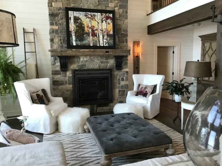A cozy living room with a stone fireplace and two white armchairs