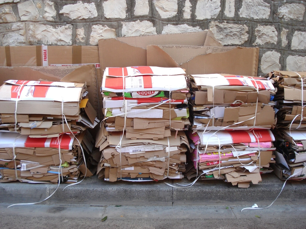 Neat bundles of flattened cardboard boxes tied with string beside a stone wall