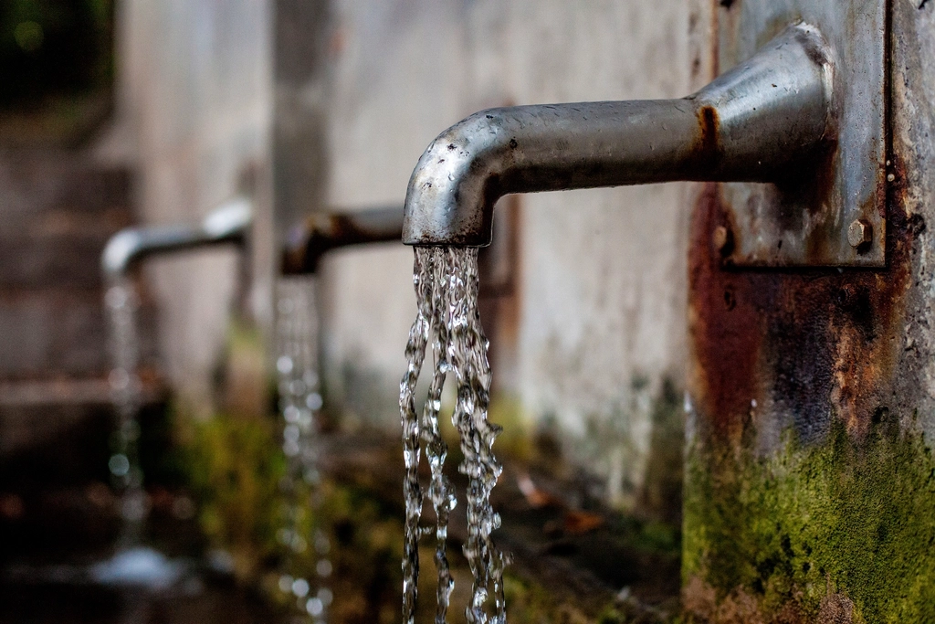 Outdoor water spigots on a wall with water trickling from them