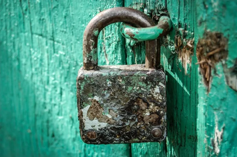 An old padlock fastened on a weathered teal wooden door