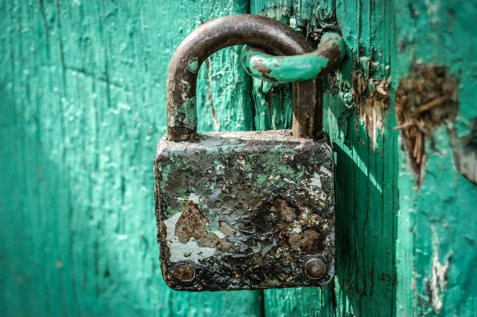 An old padlock fastened on a weathered teal wooden door