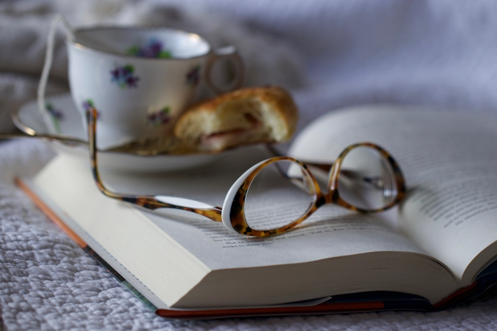 Reading glasses resting on an open book beside a teacup