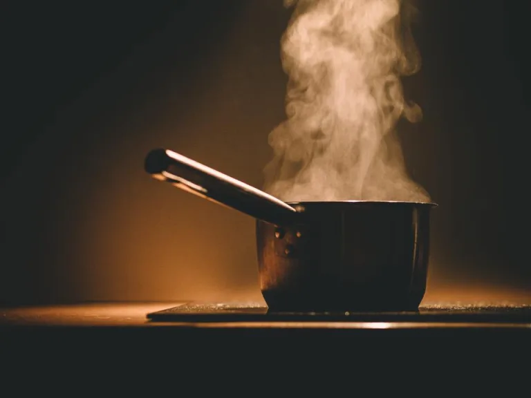 A pot on a stovetop with steam rising in warm kitchen light
