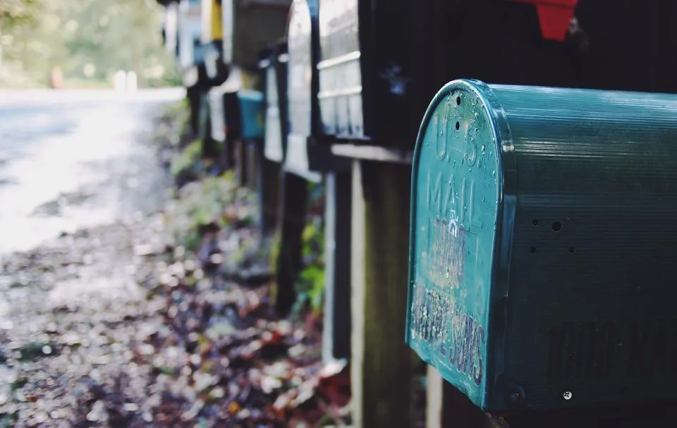 A teal rural mailbox beside a row of mailboxes along a quiet road