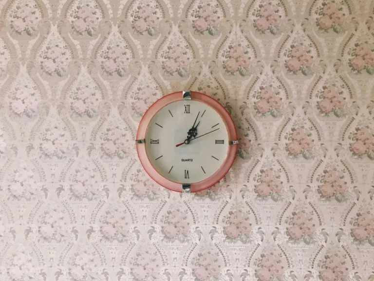 A round wall clock with a pink frame on floral wallpaper