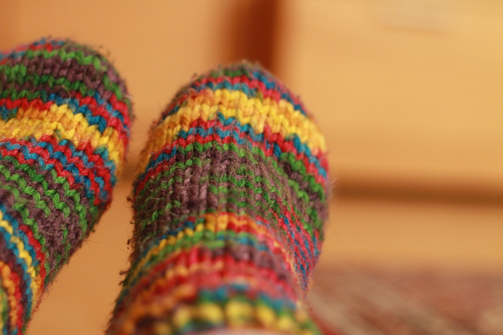 Feet in colorful striped hand-knitted wool socks in a warm room